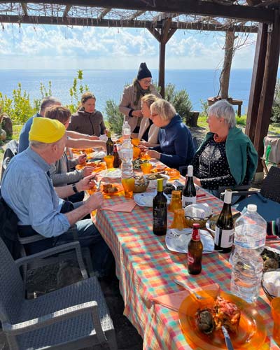 Menschen sitzen an einem gedeckten Tisch im Freien und genießen gemeinsam ein Essen mit Blick auf das Meer in Süditalien.