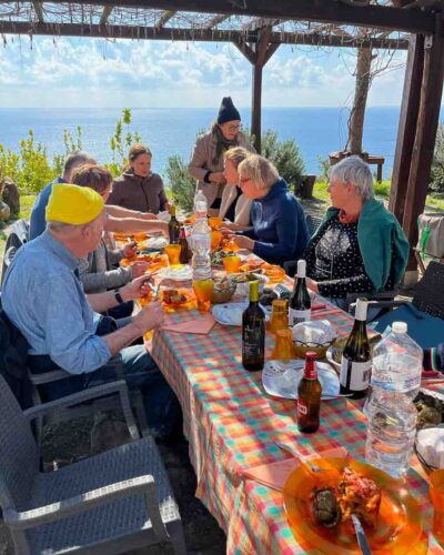 Gruppe isst bei der Zitronenernte in Italien an langer Tafel mit Blick aufs Meer
